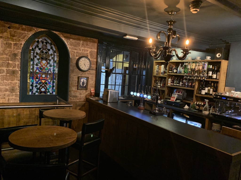 The Silk House main bar, full counter view with taps, chandelier and original stained glass