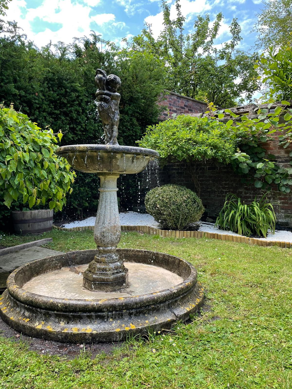 Stone fountain in The Silk House garden, surrounded by planting