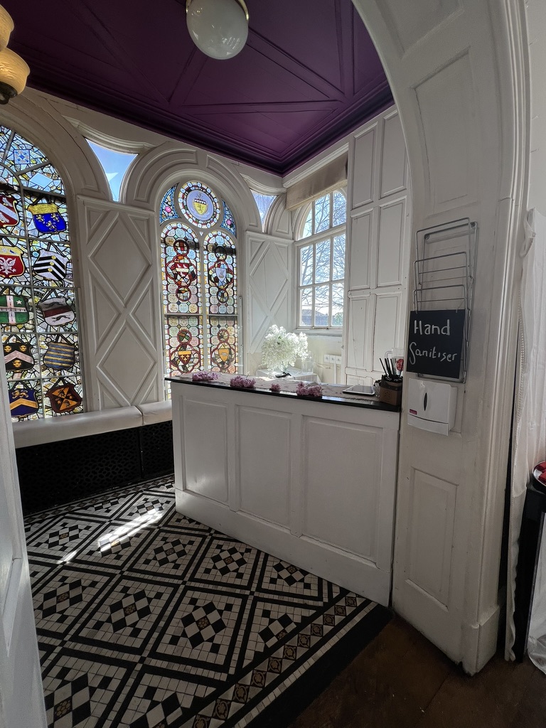 Reception desk beneath original stained glass windows and a deep purple ceiling, dressed with flowers