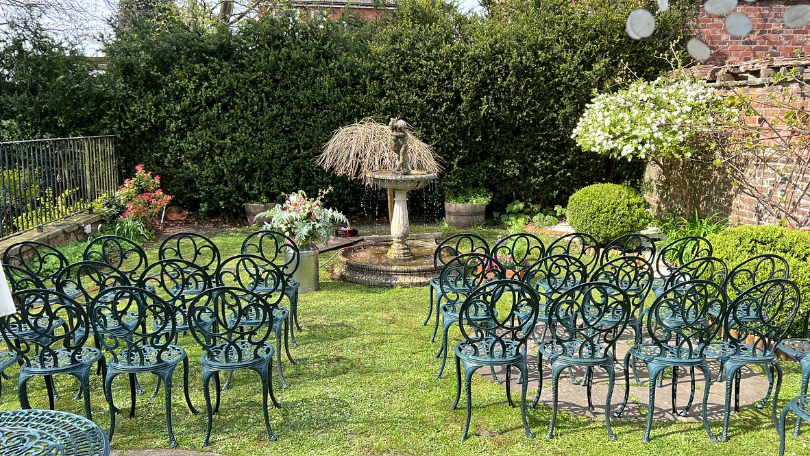 Chairs arranged for a wedding ceremony around the fountain in The Silk House's walled garden